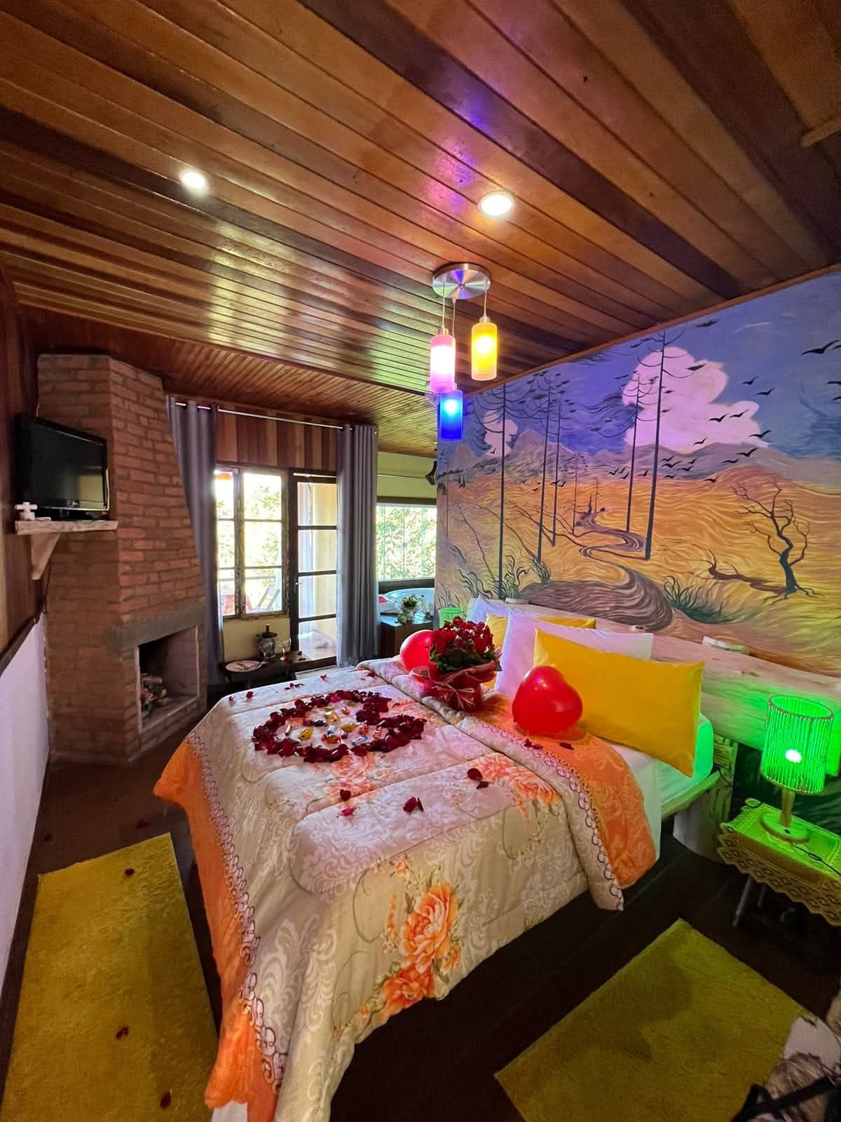 Chalé Amarelo — quarto com mural pintado do pôr-do-sol e lareira de tijolos