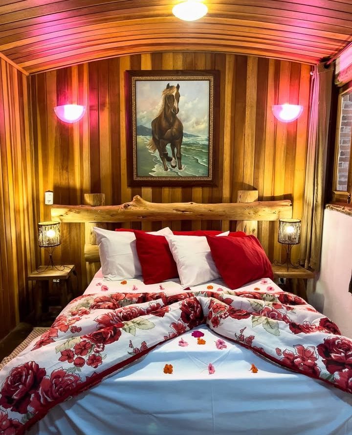 Chalé Vermelho — cama com colcha floral vermelha, quadro de cavalo e teto em madeira